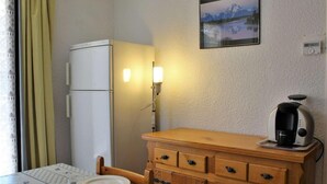 Una cocina pequeña con un refrigerador, un mueble de madera, una cafetera y una mesa de comedor con sillas.