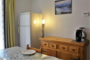 Una cocina pequeña con un refrigerador, un mueble de madera, una cafetera y una mesa de comedor con sillas.