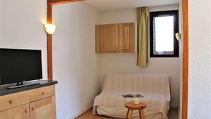 Una habitación pequeña con una cama, un televisor sobre una cómoda, una ventana con cortinas y armarios de madera.