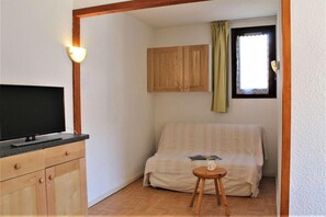 Una habitación pequeña con una cama, un televisor sobre una cómoda, una ventana con cortinas y armarios de madera.