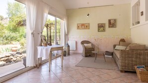 Un amplio salón con un gran ventanal, un sofá de mimbre, una mesita y una silla.