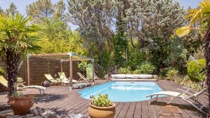 Una terraza de madera con piscina, sillas de descanso y un pérgola.