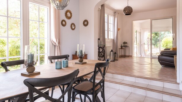 Un comedor espacioso con una mesa de madera, sillas negras y adornos decorativos. Cuenta con ventanas amplias que permiten la entrada de luz natural y vistas al exterior.