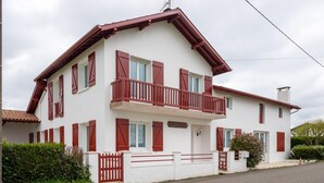 Una casa de dos plantas con balcón, fachada blanca y contraventanas rojas.