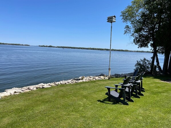A lakeside setting with a picnic table and chairs, a birdhouse on a pole, and a rocky shoreline.