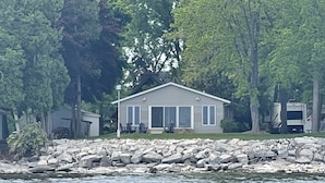 A single-story house with a front porch, situated by a rocky shoreline. - Waterfront Island-View Retreat on Rileys Point - Private Door County Escape (Sturgeon Bay)
