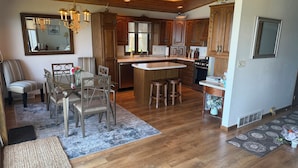 A spacious kitchen with wooden cabinets, a central island, and a dining area with a table and chairs. - Waterfront Island-View Retreat on Rileys Point - Private Door County Escape (Sturgeon Bay)
