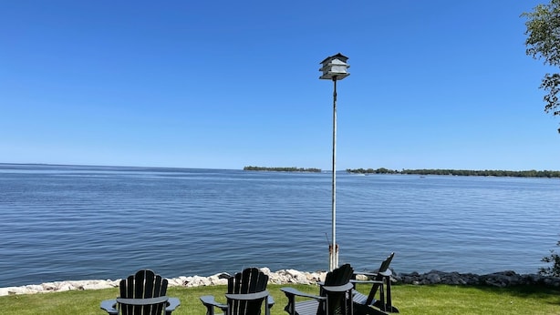 A grassy area with four Adirondack chairs facing a body of water, a tall lamp post, and a distant shoreline with trees. - Waterfront Island-View Retreat on Rileys Point - Private Door County Escape (Sturgeon Bay)