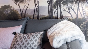 A sofa with patterned cushions and a fur throw, set against a wall mural of trees.