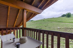 Eine Holzdar Terrasse mit Tisch und Stühlen, mit Blick auf ein Wiesenfeld mit Bäumen.