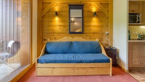 A wooden room with a bed, a small cabinet, and a kitchenette.