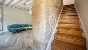 Eine Treppe mit Holzbodenstufen führt zu einer Zwischenebene, einem Steinpfeiler und einem türkisfarbenen Sofa mit Kissen.