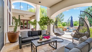 A spacious patio with a black sofa, a hanging chair, and a coffee table with decorative items. - ❤️️3 Min to Old Town❤️️Spectular Villa❤️️SwimBar❤️️PickleBall❤️️Golf❤️️Spa❤️️BBQ (Scottsdale)