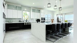 A modern kitchen with white cabinetry, a marble island, and black bar stools.