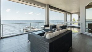 A balcony with wicker furniture, a view of the water, and a dining area.