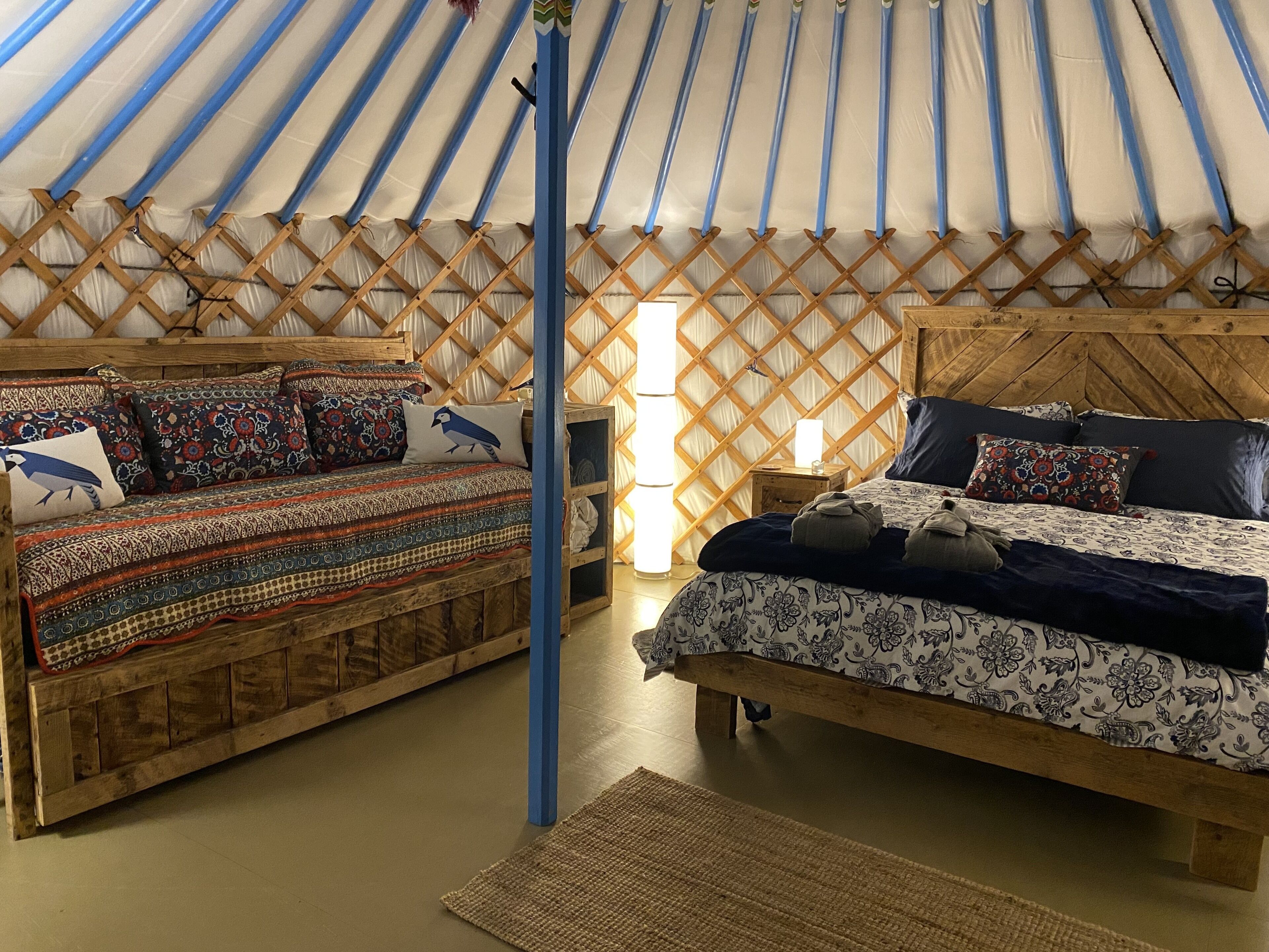 A cozy interior with two beds, a wooden bench, and a small table with a lamp.