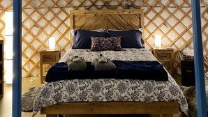 Interior tradicional de una yurta con una cama de madera, almohadas y un edredón estampado.