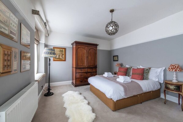 Een slaapkamer met een groot bed, een houten garderobe, een radiator en kunst aan de muur.