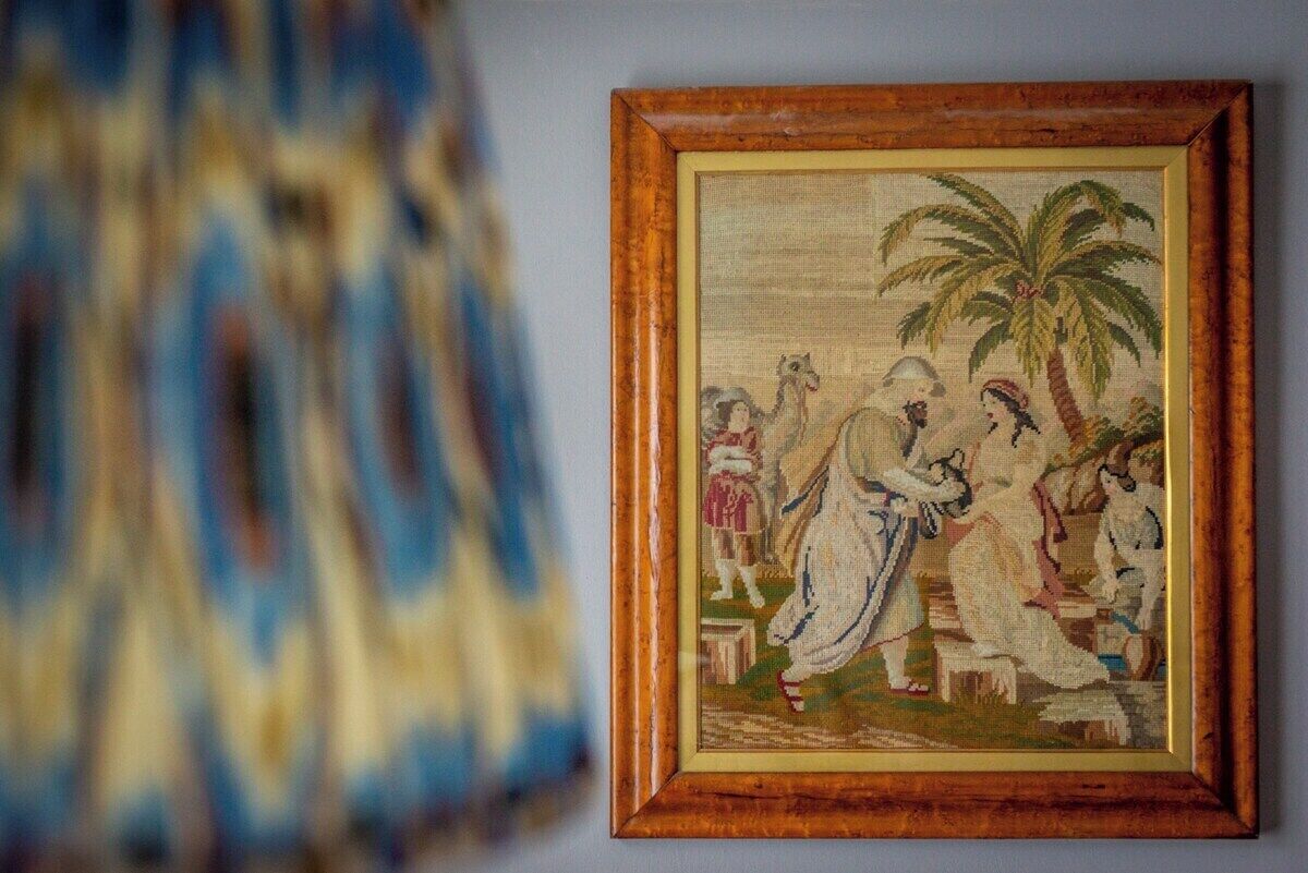 A framed cross-stitch artwork depicting a tropical scene with palm trees and people.