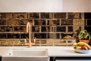 Een keuken met een wit spoelgedeelte, een koperen kraan en een backsplash van mozaïek.