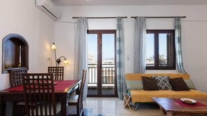 A living room with a sofa, a dining table with chairs, a small table with a plate, and a window with curtains. - Beautiful 2-bed Apartment in Rethymno (Rethymno)