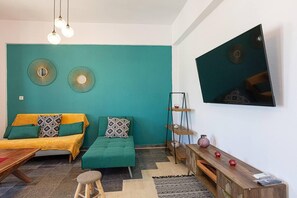 A living room with teal walls, a sofa, a coffee table, a TV, and a small wooden cabinet.