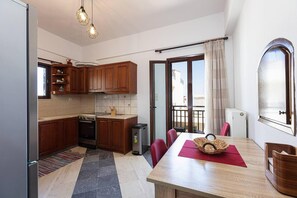 A compact kitchen with wooden cabinets, a dining table with chairs, and a view of the outside through a sliding glass door.