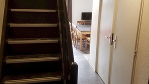 Eine Treppe führt zu einem Raum mit einem Flachbildfernseher, Holzmöbeln und einer Tür mit Griff.