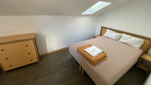 Ein Schlafzimmer mit einem Bett, einem Nachttisch, einer Kommode und einem Oberlicht.