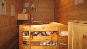Une chambre dans un chalet en bois, avec un lit superposé, un petit bureau et une lampe.