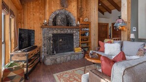 L’intérieur chaleureux d’un chalet avec une cheminée en pierre, des murs en bois, un téléviseur et un canapé.