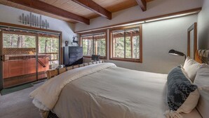 Une chambre avec un grand lit, des poutres apparentes en bois au plafond et une vue sur une terrasse en bois, accessible par une porte-fenêtre coulissante.