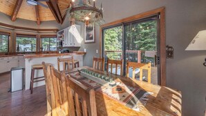 Une cuisine spacieuse avec des poutres en bois, un grand îlot central doté de tabourets de bar et une vue sur l’extérieur grâce à de grandes fenêtres.