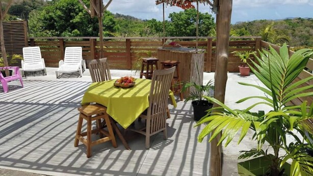 Un patio al aire libre con una mesa dispuesta para dos personas, rodeado de sillas y una mesa de madera.