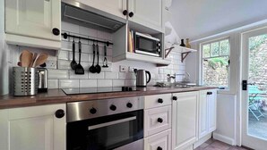 A modern kitchen with white cabinets, stainless steel appliances, and a wooden countertop. - Charming Weaver's Cottage in Historic Frome (Frome)