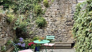 A stone wall with ivy, a round table with a green chair, and a bench. - Charming Weaver's Cottage in Historic Frome (Frome)