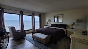 A hotel room with a large bed, a chair, a nightstand, and a view of the ocean. - The Colony Condominiums Oceanfront Unit with Amazing Oceanfront Balcony (Virginia Beach)