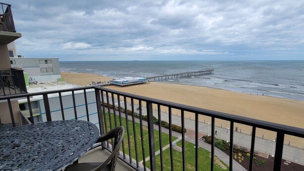 A balcony with a view of a beach, a pier, and a distant island. - The Colony Condominiums Oceanfront Unit with Amazing Oceanfront Balcony (Virginia Beach)