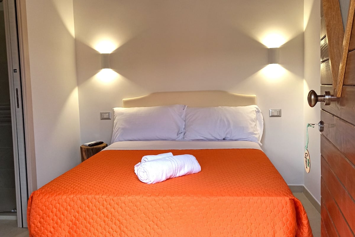 Un lit avec une couette orange, des oreillers blancs et une couverture blanche enroulée au pied du lit.