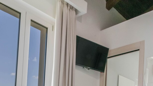 Un dormitorio con un ventanal grande, una cama, un televisor y un baño visible a través de una puerta abierta.