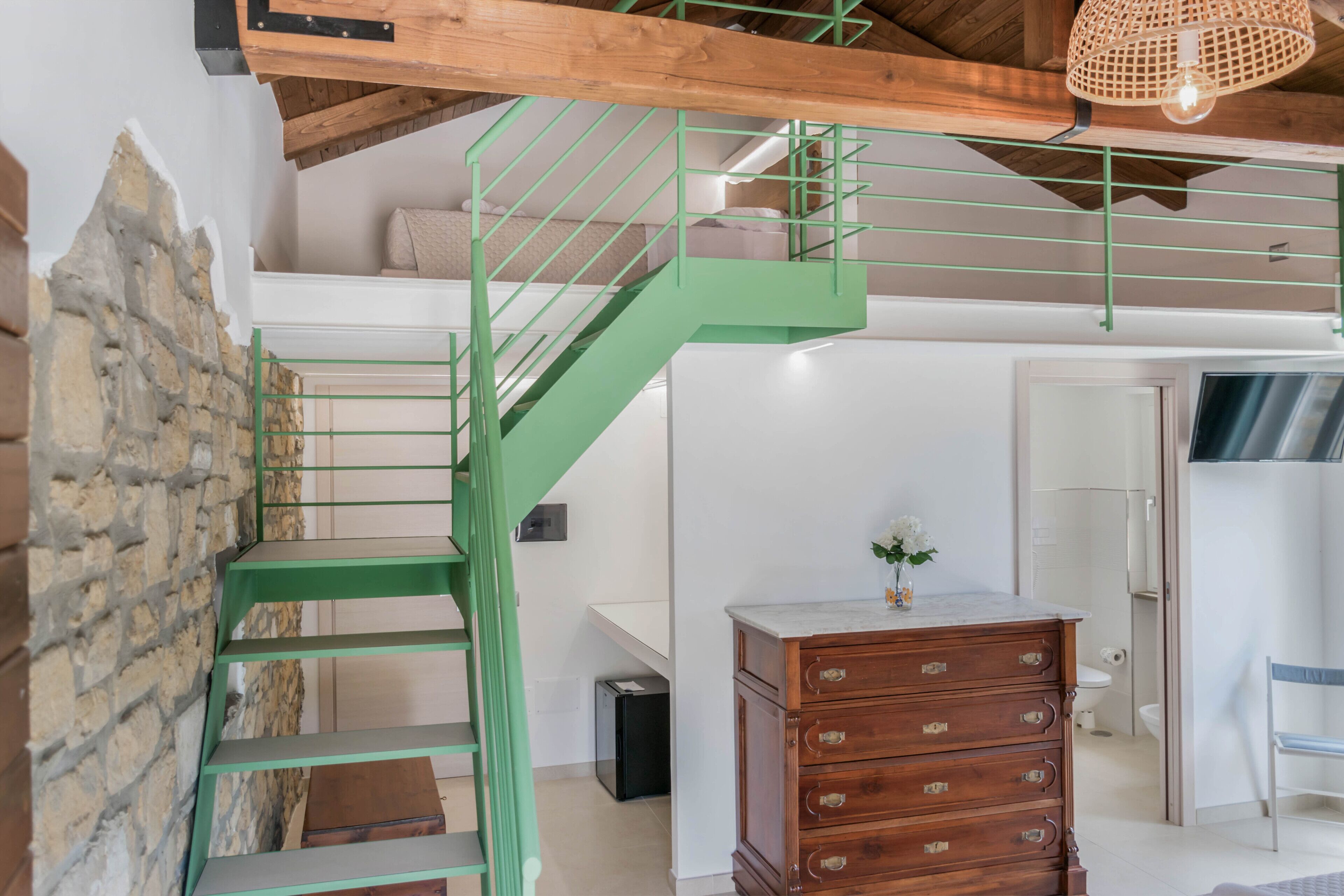 Un interno moderno con una scala in metallo verde, un comò in legno e un muro in pietra.