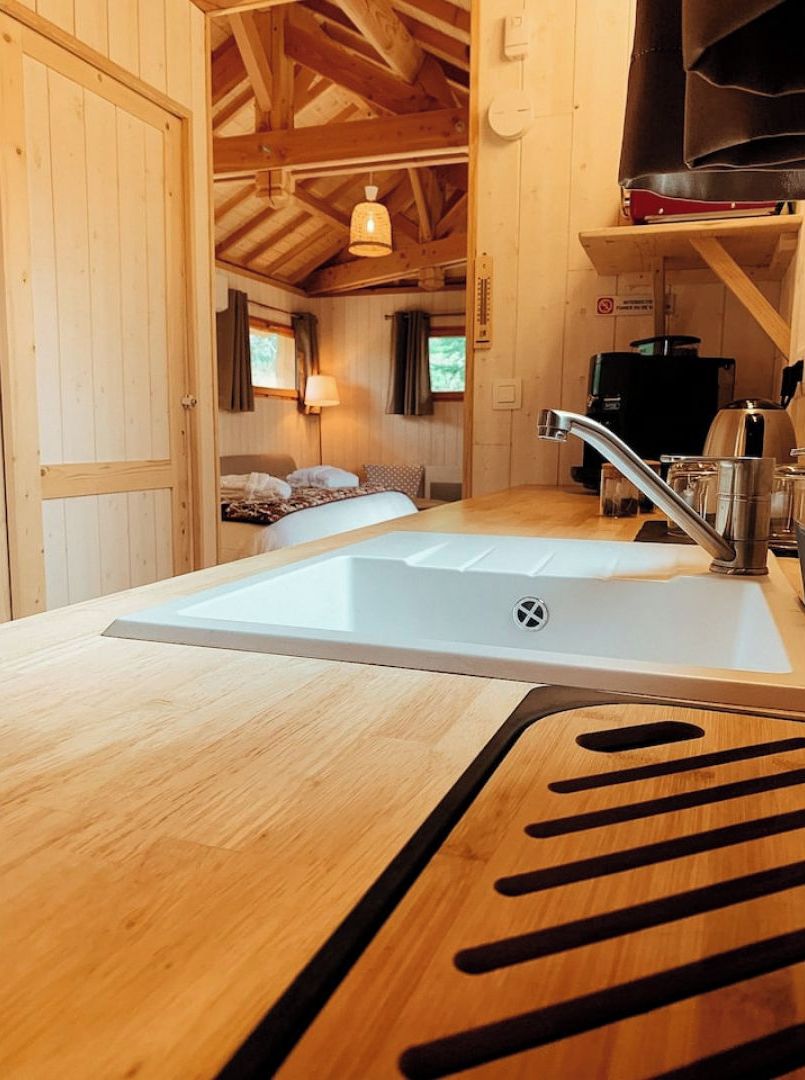 Un intérieur en bois comprenant un coin cuisine équipé d’un évier, d’une cuisinière et d’un lit donnant sur l’extérieur.