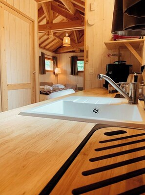 Interior de madera con cocina que incluye un lavabo, una estufa y una cama con vistas al exterior.
