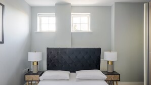 Una habitación de hotel con una cama grande, dos mesitas de noche con lámparas y dos ventanas.