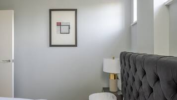 A hotel room with a neatly made bed, a framed artwork on the wall, a bedside lamp, and a window providing natural light.
