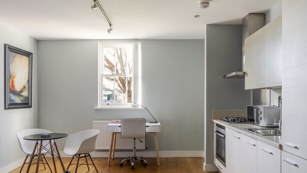 Una cocina moderna con armarios blancos, estufa a gas y microondas. Hay un comedor con dos sillas y una mesita.