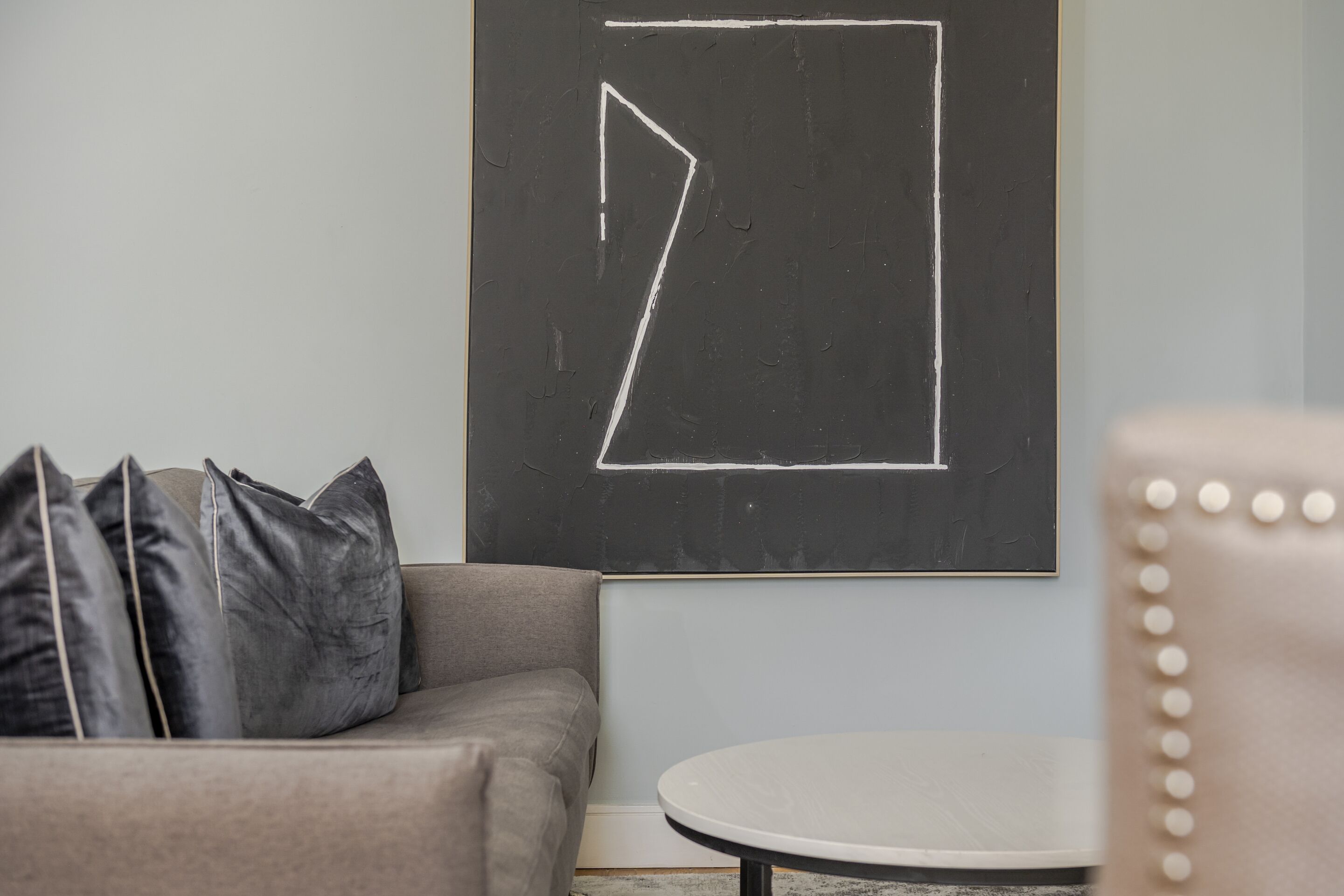 Una habitación con un sofá gris, una pequeña mesa redonda y una pared con un dibujo geométrico hecho con tiza.