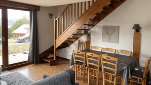 Un espace repas avec un escalier en bois, une table et des chaises, et une vue sur l’extérieur.