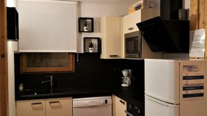 A compact kitchen with a dishwasher, stove, microwave, and refrigerator. There is a trash bin and a small sink.