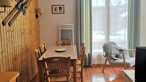 A cozy room with a wooden dining table, chairs, a TV, and a window with curtains.